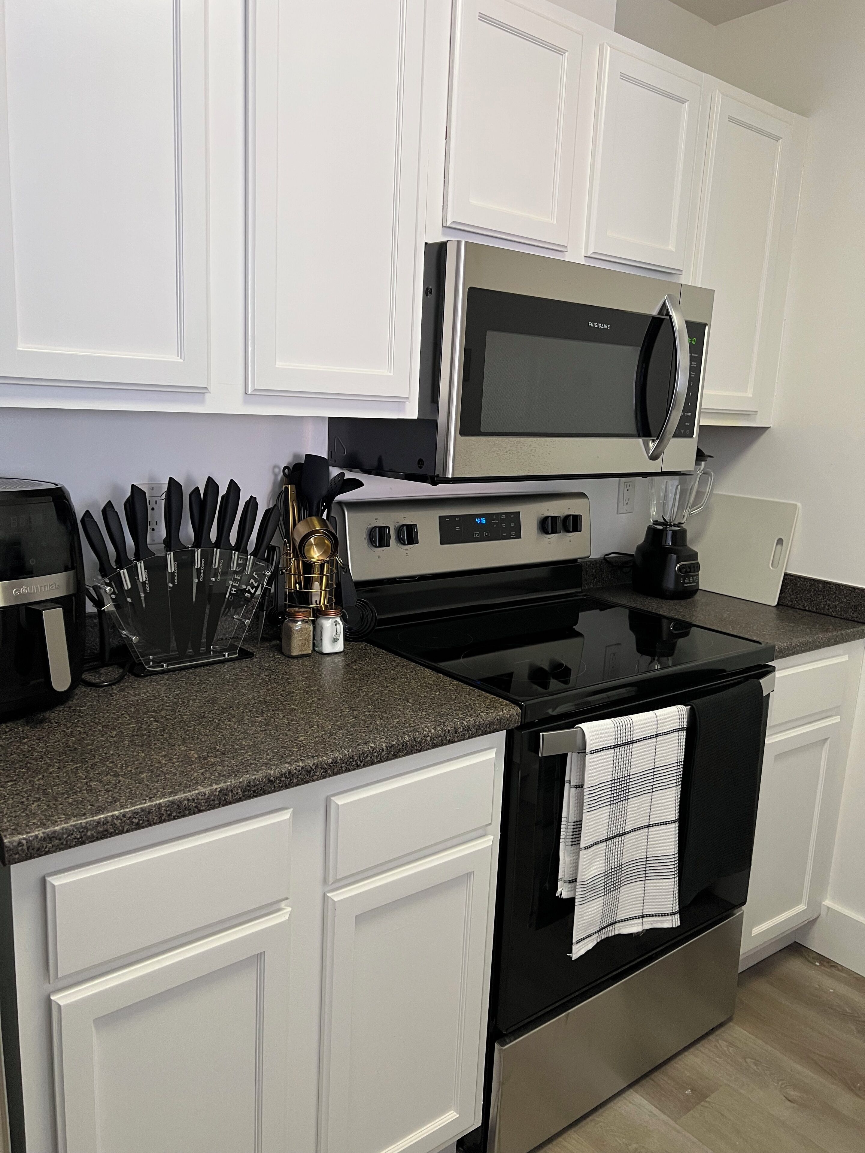A kitchen with white cabinets, a black stove, a microwave, and a coffee maker.