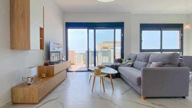 Una sala de estar moderna con un sofá gris, un mueble bajo de madera para el televisor y una pequeña mesa redonda.