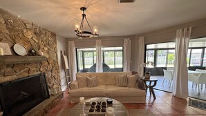 Un salon avec une cheminée en pierre, un canapé beige, une table basse en bois et un lustre.