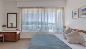 Ein Schlafzimmer mit einem großen Bett, einem Nachttisch, einem Spiegel und einem Fenster mit transparenten Vorhängen.