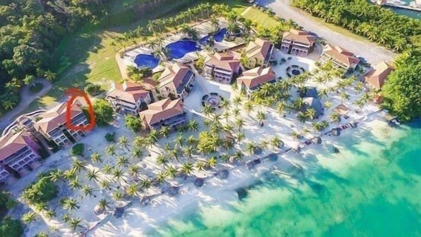 An aerial view of a resort with multiple buildings, palm trees, and a large body of water. - Beach Front Condo steps from beach (Roatan)
