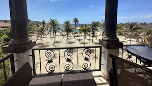 A balcony with a view of a beach, palm trees, and a clear sky. - Beach Front Condo steps from beach (Roatan)
