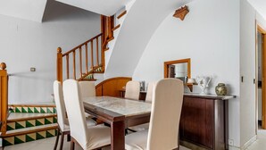 Un coin repas avec une table et des chaises en bois, un escalier et un petit meuble contenant des objets décoratifs.