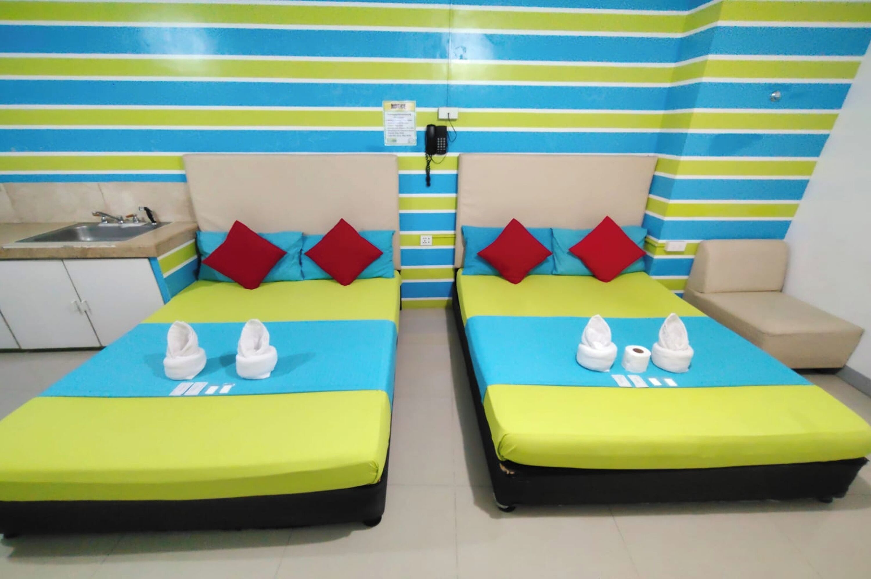 A hotel room with two beds, a sink, a telephone, and a striped wall.