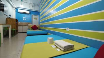 A room with striped walls, a bed with a yellow mattress, a red pillow, a white towel, and a toilet paper roll.