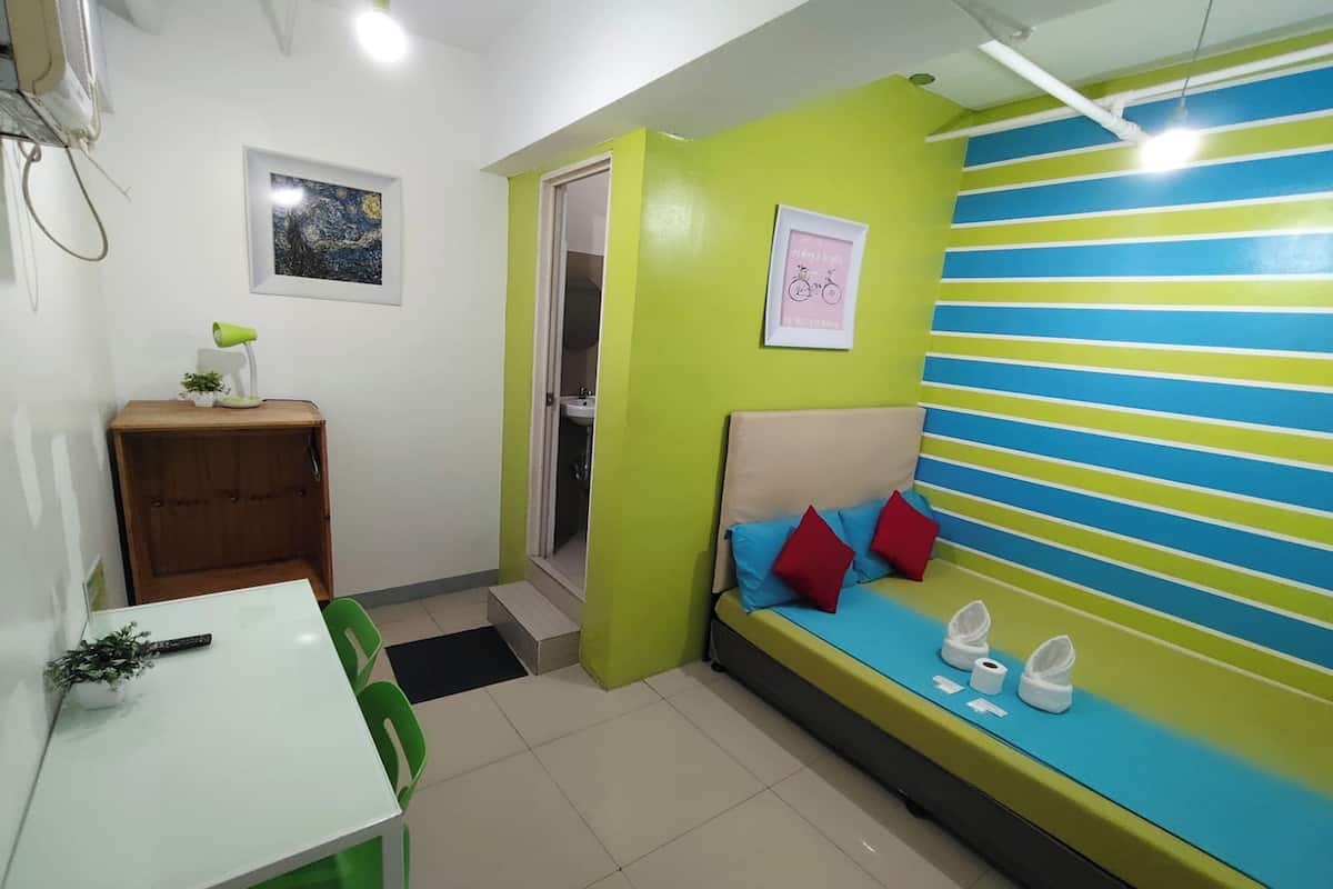 A room with a bed, a table with chairs, a small cabinet, and a door leading to a bathroom.