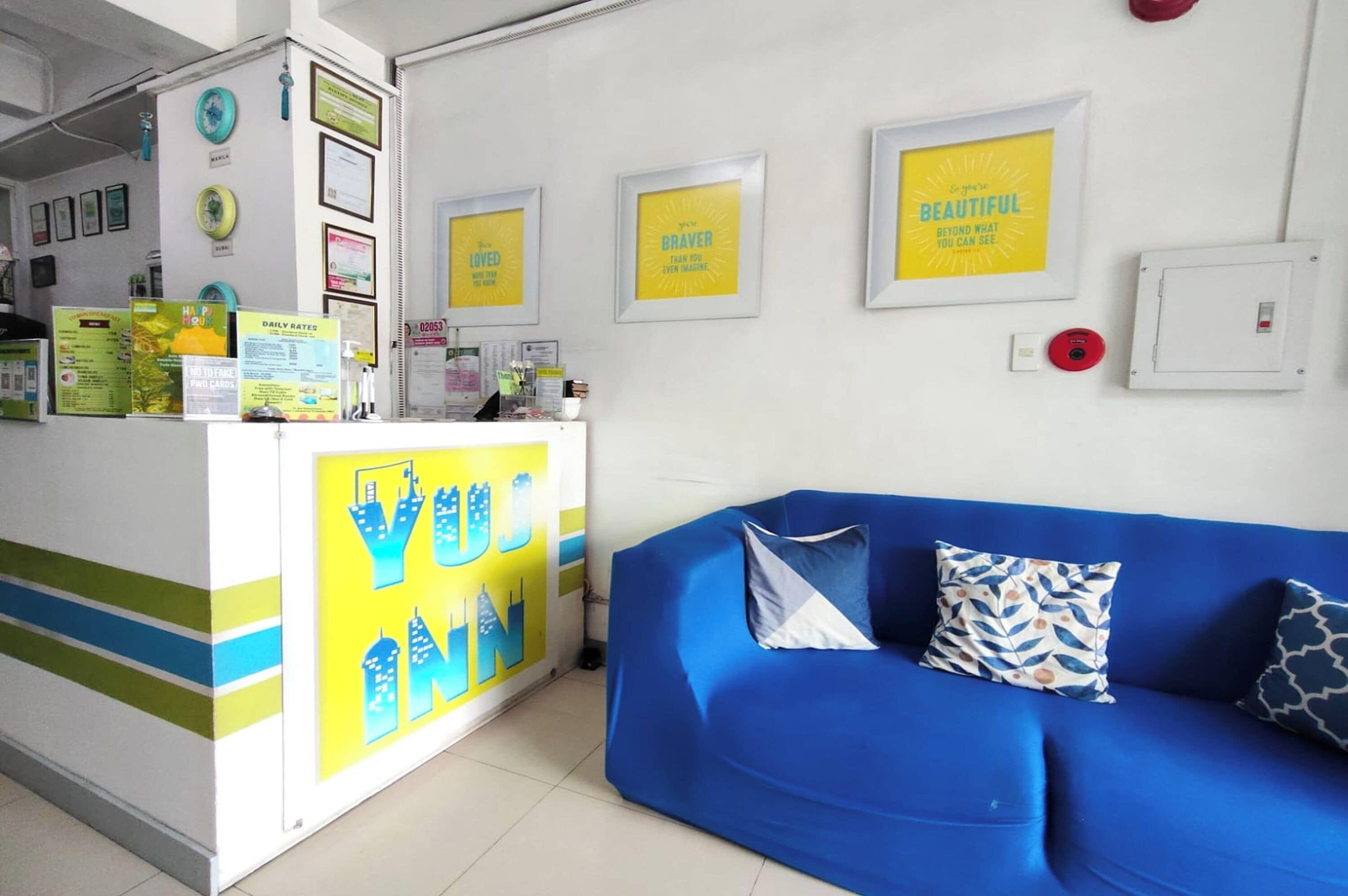 A reception desk with framed motivational quotes, a blue sofa with patterned cushions, and a tiled floor.
