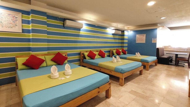 Quarto de hotel com paredes listradas, várias camas e uma pequena mesa com cadeiras.
