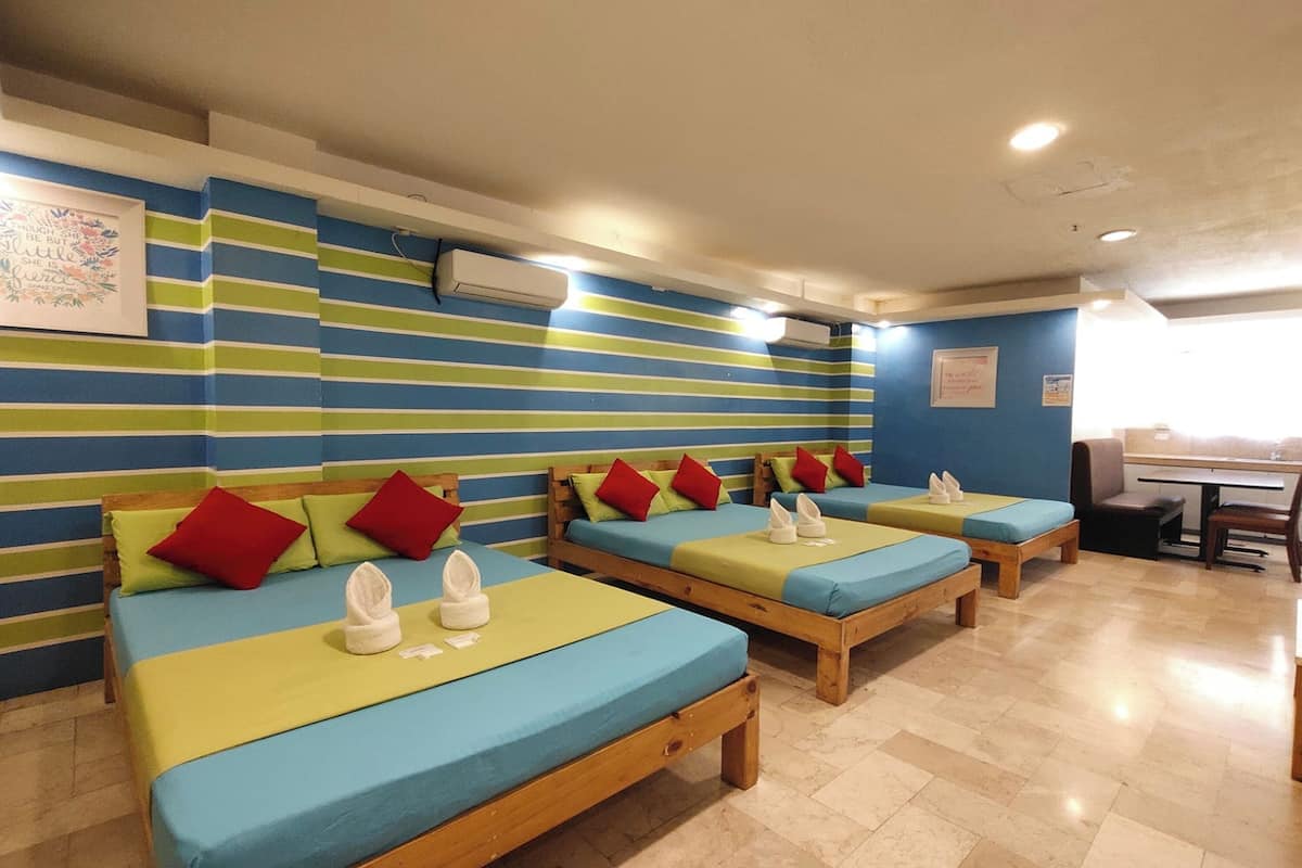 A hotel room with striped walls, multiple beds, and a small table with chairs.