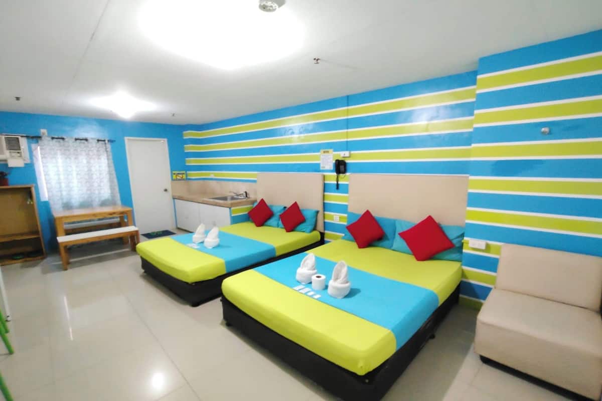 A hotel room with two beds, a bench, a chair, and a small kitchenette.