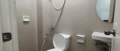 Un baño con inodoro, ducha, lavamanos y espejo.