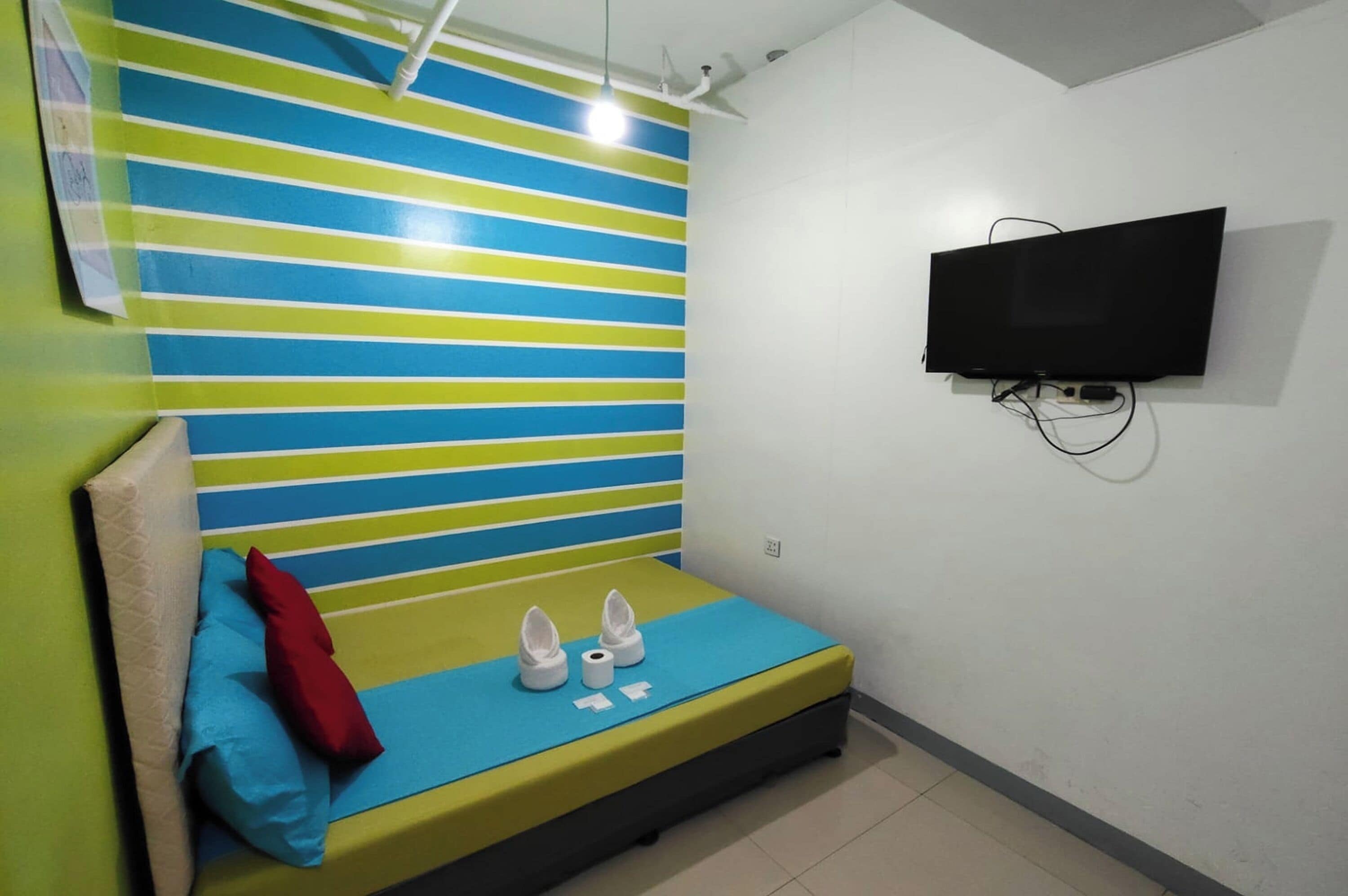 Una habitación pequeña con una cama, un televisor fijado a la pared y un papel tapiz a rayas.