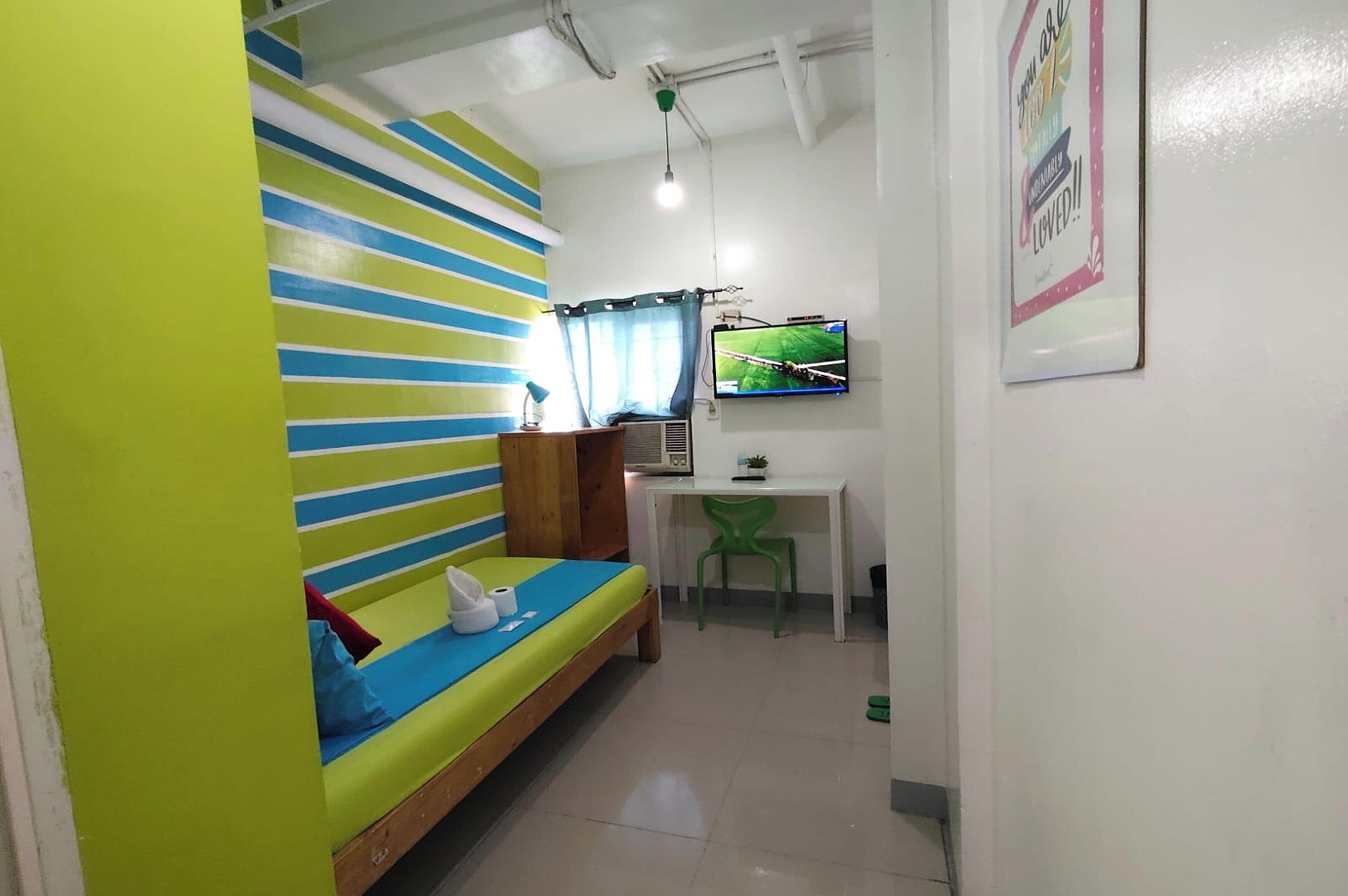 A room with a bunk bed, a desk with a chair, a television, and a poster on the wall.