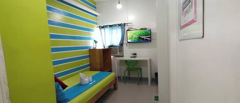 Una habitación con literas, un escritorio con silla, un televisor y un cartel en la pared.