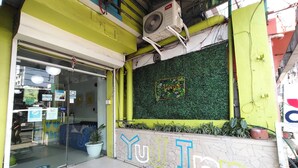 Entrada de um edifício com porta de vidro, parede verde com padrão decorativo e um letreiro com as letras 'YU' no chão.