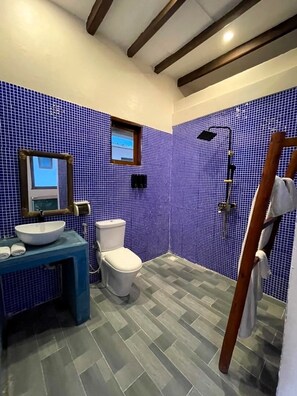 Une salle de bain avec un mur recouvert de carreaux bleus, un lavabo blanc, des toilettes et un espace douche.