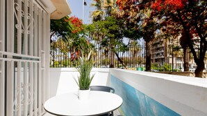 A balcony with a round table and two chairs, a potted plant, and a view of a cityscape with palm trees and buildings. - 101 Playa Honda, Playa de las Americas (Playa de las Américas)