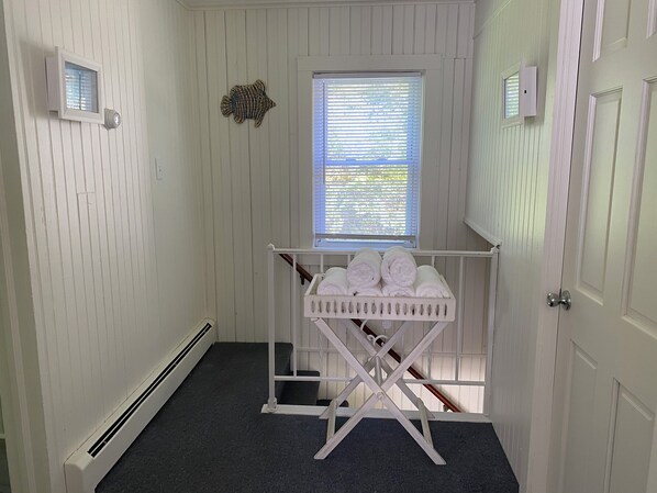 A room with white paneled walls, a window with blinds, a radiator, and a white crib with rolled towels. - The Farmhouse on Martin Lane (Rehoboth Beach)