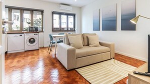 Un espacio habitable compacto con kitchenette, sofá, comedor y un gran ventanal que proporciona luz natural.