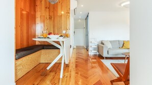Un intérieur moderne avec un mur d’accent en bois, une table à manger blanche agrémentée d’un saladier de fruits et de verres, et un canapé gris dans une pièce lumineuse dotée d’un plancher en bois.