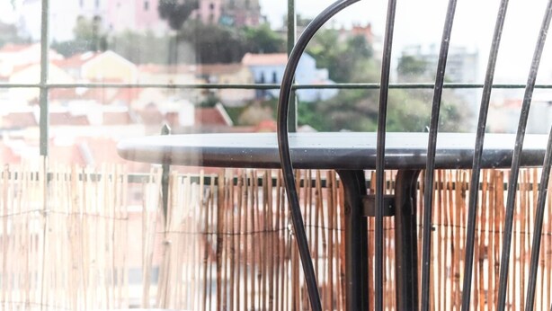 Un balcon avec une chaise et une table en métal, donnant sur un paysage urbain avec des immeubles et une tour.