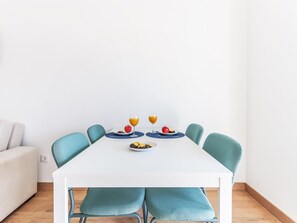 A dining table with four chairs, two plates with food and drinks, and a white wall in the background. - Vita Portucale | Almada Balcony (Almada)