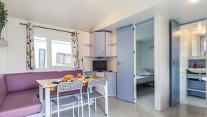 Ein gemütlicher Raum mit violettem Sofa, einem kleinen Esstisch mit Stühlen, einem Fernseher, einem Bett und einem Badezimmer mit Waschbecken und Spiegel.