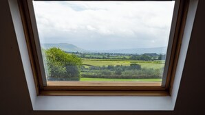 Une lucarne offrant une vue sur un paysage verdoyant, avec des champs et des collines à l’horizon.