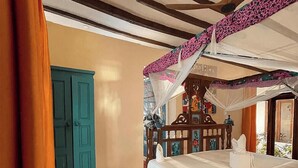A bedroom with a bed, a wooden headboard, a nightstand, a blue door, and a red carpet. - Asante Sana Beach Cottages - Beachfront Cottage (Fukuchani)