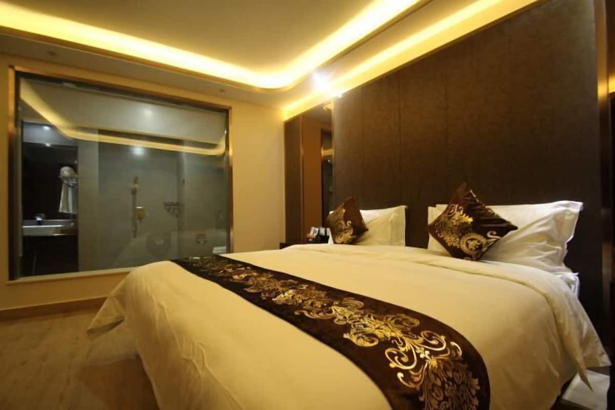 Habitación de hotel con una cama grande, zona de ducha con mampara de cristal y cabecero de madera oscura.