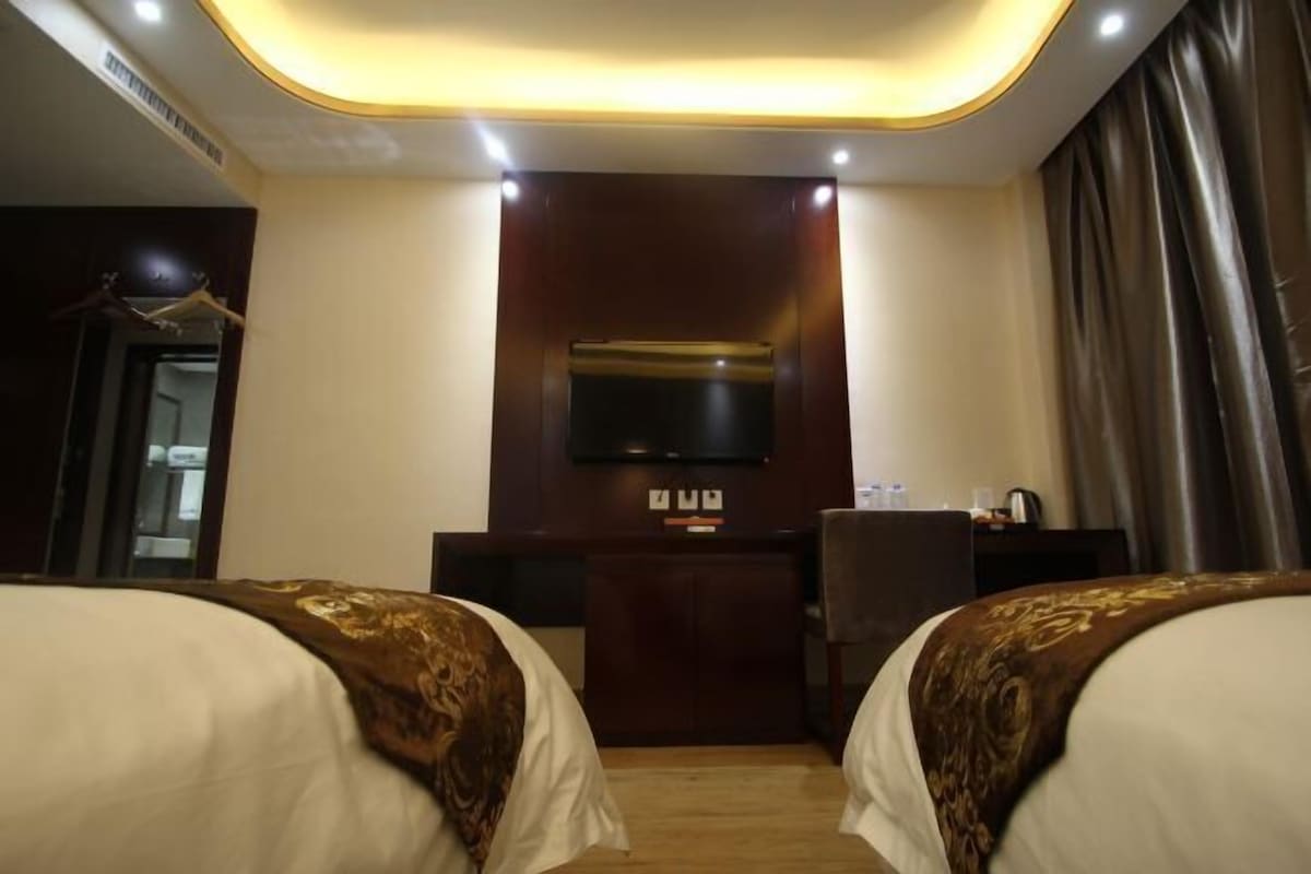 A hotel room with two beds, a flat-screen TV mounted on the wall, a desk with a chair, and a wardrobe.