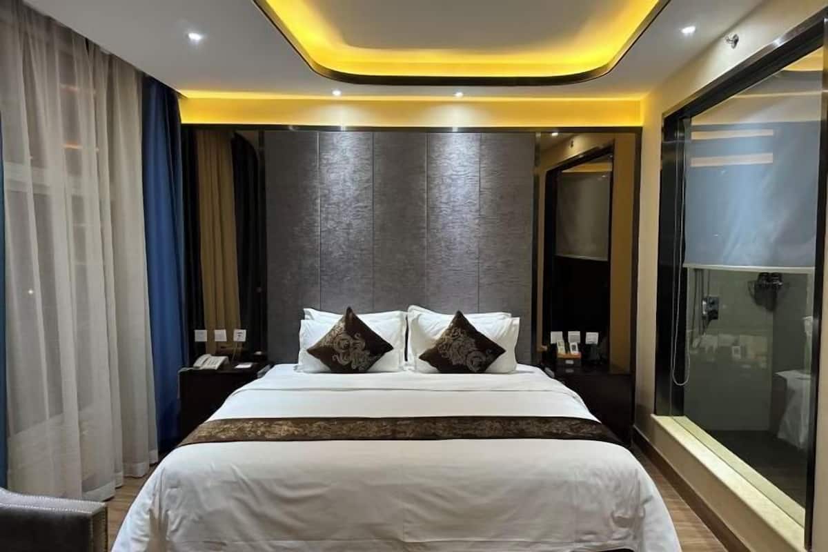 Habitación de hotel moderna con una cama grande, cabina de ducha de vidrio y una pared oscura con textura.