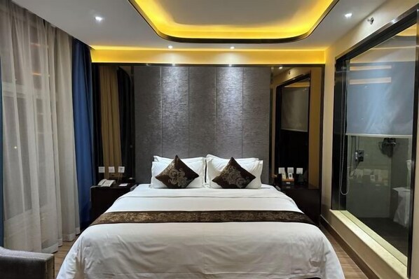 A modern hotel room with a large bed, a glass shower enclosure, and a dark textured wall. - Chunguang Hotel (Xiji)
