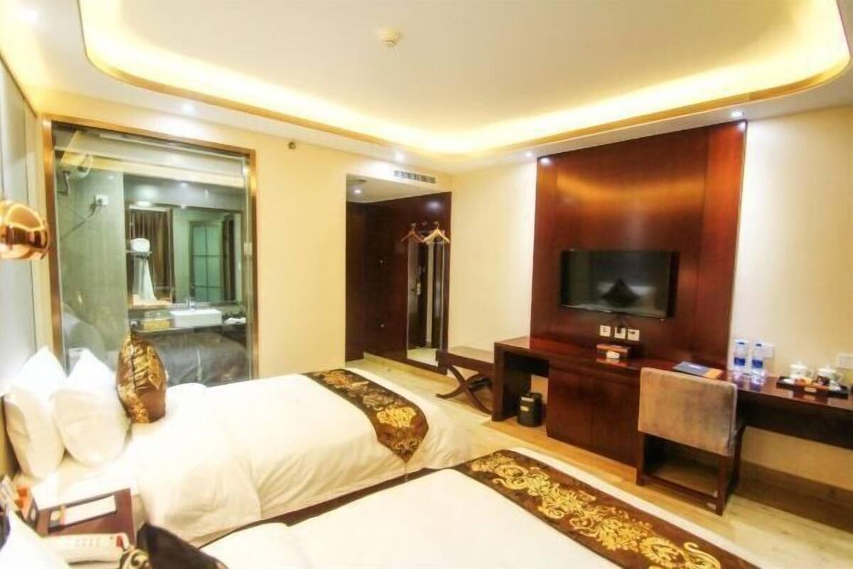 Habitación de hotel con dos camas, televisión, escritorio y espejo.