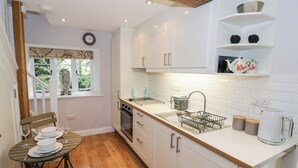 Cocina pequeña con armarios blancos, encimera de madera y ventana con vistas a la vegetación.