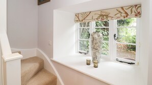 Una habitación con un asiento junto a la ventana, un jarrón grande y dos velas pequeñas.