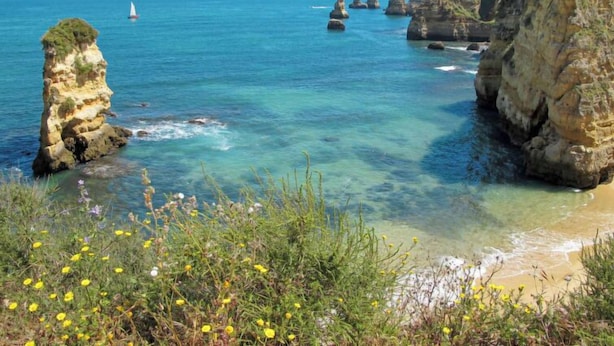 A coastal landscape with clear waters, rocky formations, and a sailboat in the distance. - Dona Ana by Interhome (Lagos)