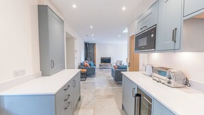 A modern kitchen with grey cabinets, a microwave, and a toaster. There is a seating area with a sofa and a TV in the background. - No 2 The Coach House (Carnforth)