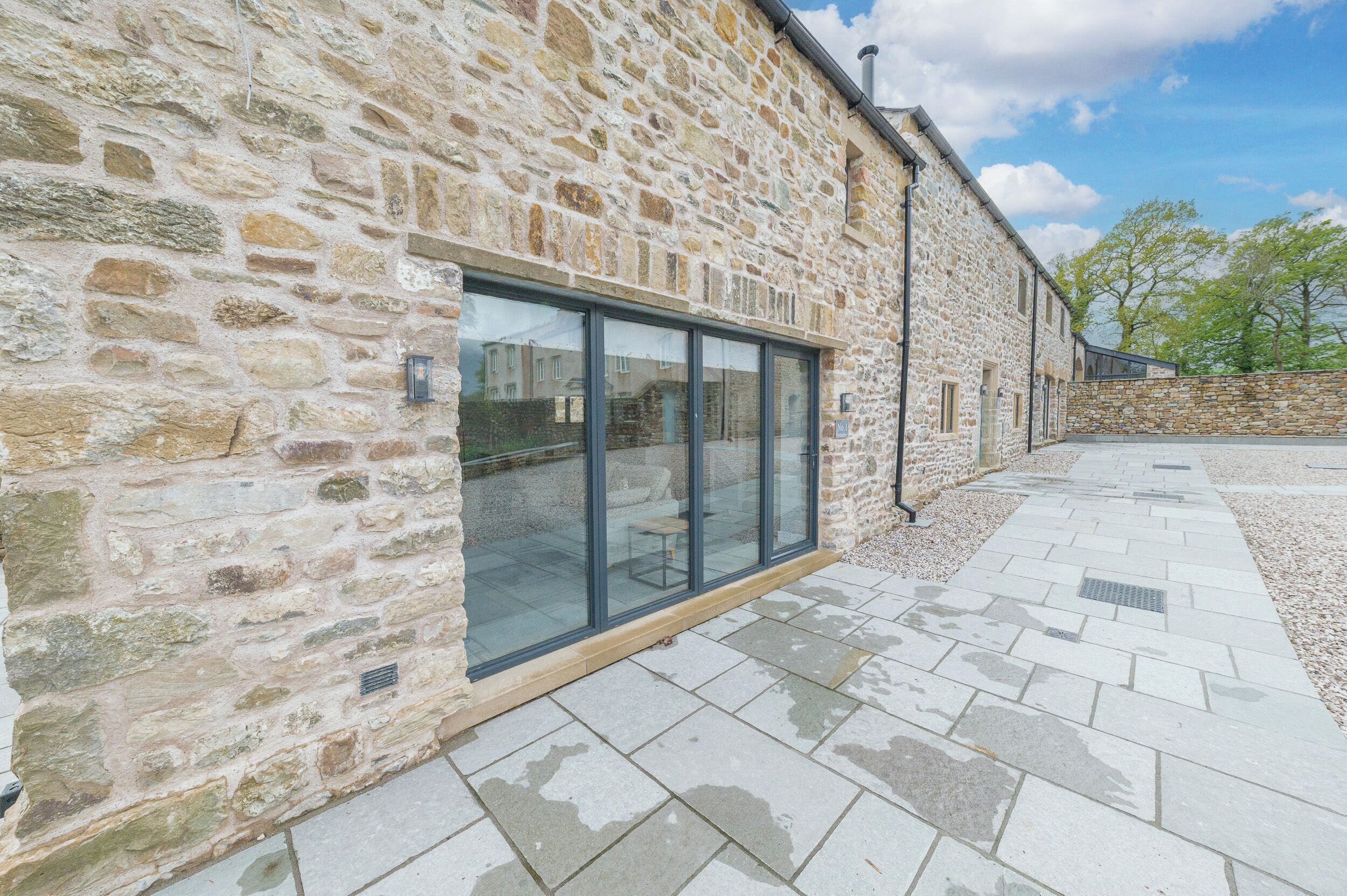 A stone building with large glass windows and a paved patio area.