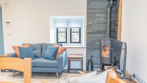 A cozy living room with a grey sofa, a small wooden table, and a black fireplace. - No 2 The Coach House (Carnforth)