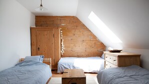 Une chambre avec deux lits, une armoire en bois, une commode et une lucarne.