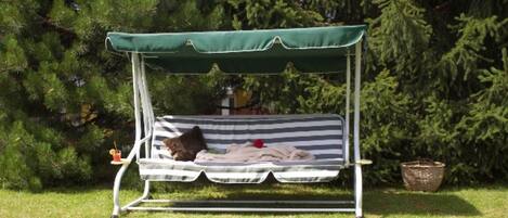 A garden swing with a striped cushion and a green canopy, surrounded by grass and trees.