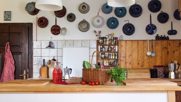 Une cuisine avec un comptoir en bois, des assiettes suspendues, un panier rempli de légumes et une étagère avec des bocaux.