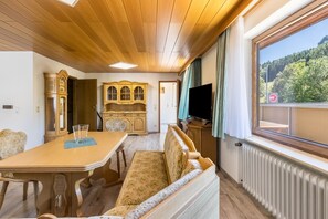 Une pièce avec un plafond en bois, une table à manger avec des chaises, un canapé, un téléviseur et une fenêtre donnant sur des arbres.