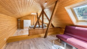 Un interior de madera con techo inclinado, una mesa de vidrio, un sofá morado y una ventana con vistas a árboles.