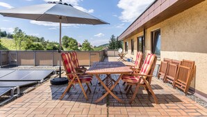 Un patio exterior con una mesa, sillas, paneles solares y un gran paraguas.