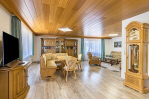 Un salon doté d’un parquet, d’un téléviseur, d’une table à manger avec des chaises, d’un canapé et d’une grande armoire en bois.