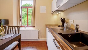 Una cucina compatta con finestra, mobili bianchi, un lavandino e un'area pranzo con tavolo e sedie.