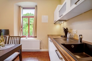 Una cocina compacta con ventana, armarios blancos, un lavamanos y una zona de comedor con mesa y sillas.