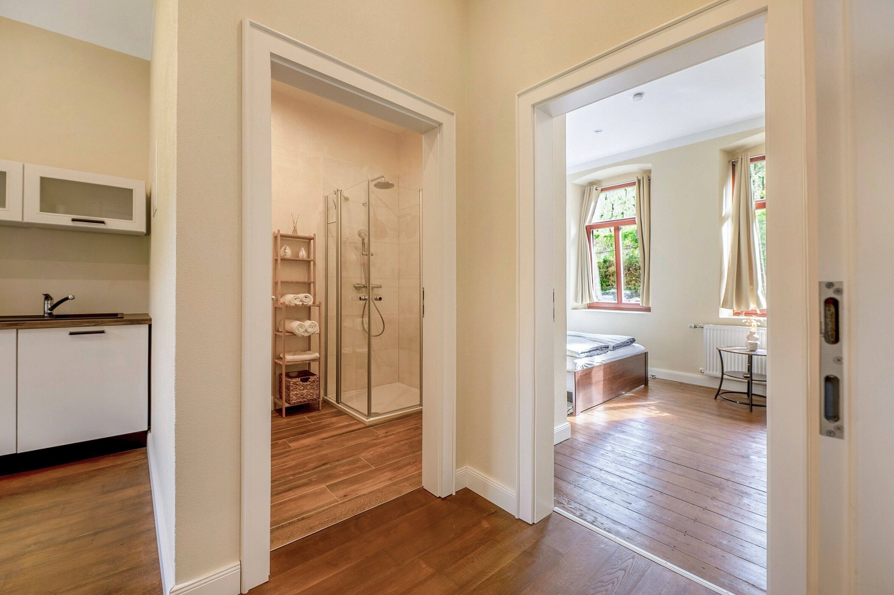 Ein modernes Badezimmer mit Glasdusche, Holzboden und Gartenblick durch ein Fenster.
